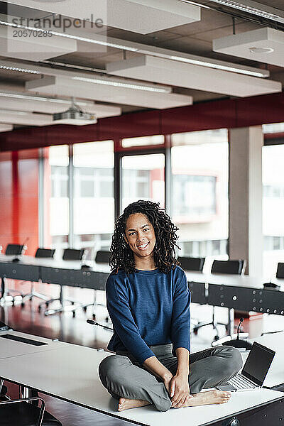 Smiling young businesswoman sitting cross-legged on conference table at office