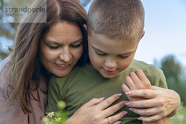 A mother hugs her son and holds his hand.