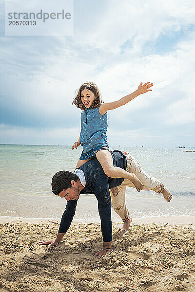 Cheerful girl enjoying piggyback ride in front of sea