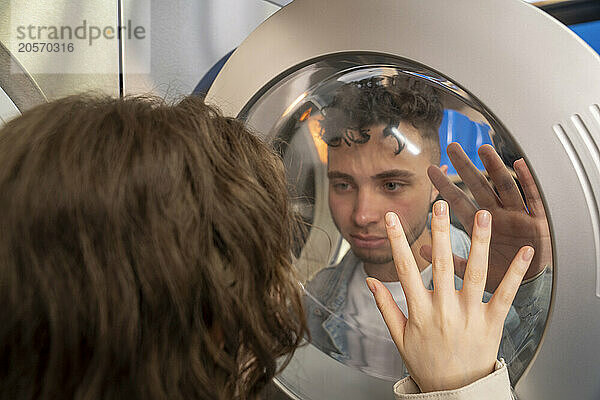 Young couple looking through washing machine glass at laundromat