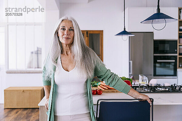 Smiling mature woman with gray hair standing in kitchen at home