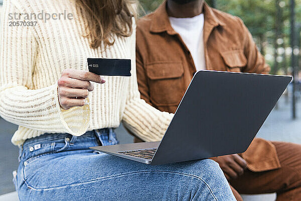 Woman with credit card using laptop sitting by boyfriend