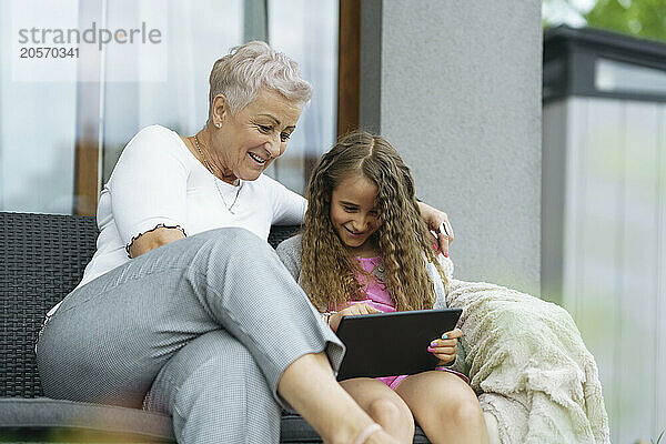 Happy grandmother with cute granddaughter using tablet PC at patio