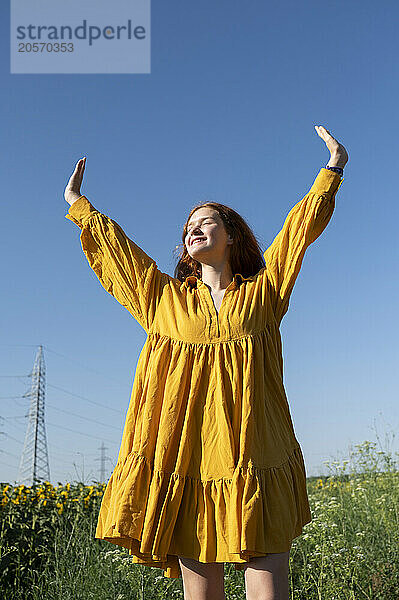 Teenage girl with red hair in a yellow dress in a field on the blue sky background