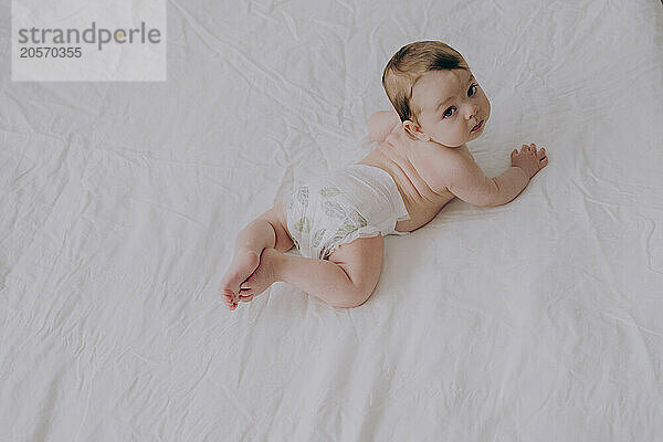 Cute baby boy in diaper lying on bed at home