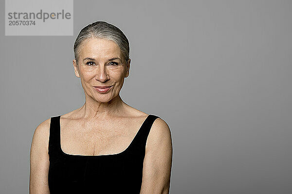 Smiling senior woman in black sportswear against gray background