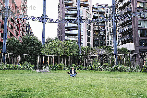 Businesswoman meditating on grass at office park