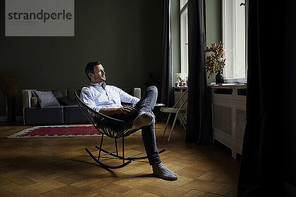 Thoughtful man sitting on rocking chair with legs crossed at knee in home