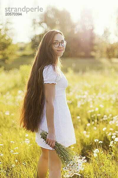 Smiling young woman with long hair standing in chamomile field