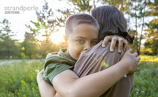 A boy hugs his mother in the park.