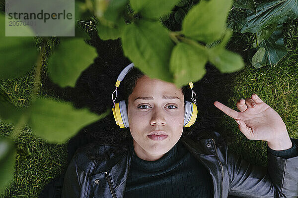 Young woman listening to music through wireless headphones lying near green plants at park