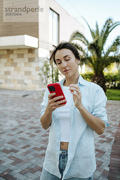 Woman using smart phone standing in back yard