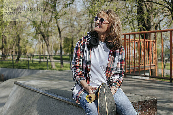 Senior woman sitting with skateboard in park