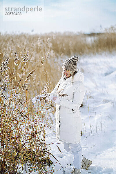 Woman in warm clothes standing near dried plants on snow