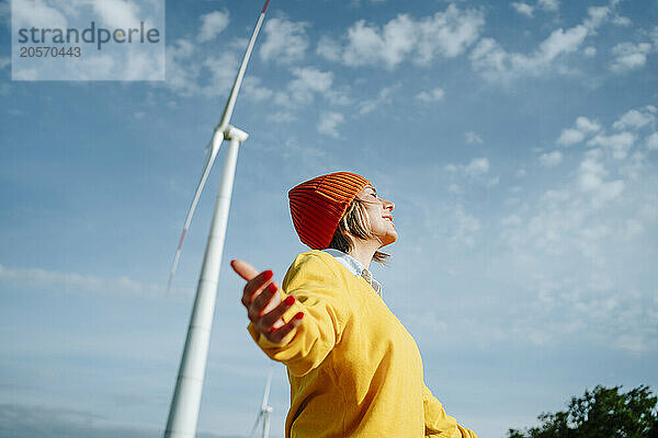 Happy woman with arms outstretched standing under blue sky