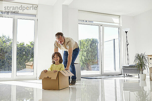 Father pushing son in cardboard box at new empty house