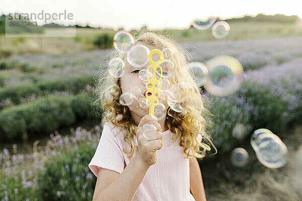 Playful girl blowing bubbles and standing in lavender field