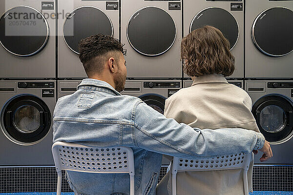 Couple sitting on chairs waiting at laundromat