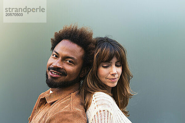 Smiling man standing back to back with girlfriend against gray background