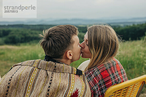 Romantic young couple kissing and sitting on chair at meadow on mountain of Poland