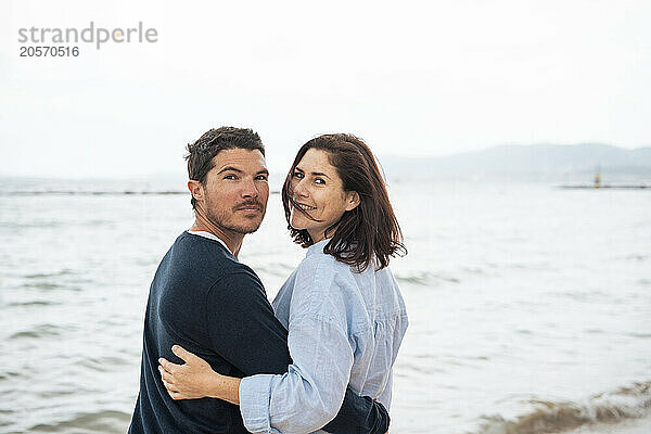 Smiling man and woman standing together in front of sea at beach