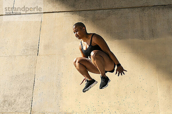 Determined sporty woman jumping in front of wall