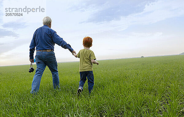 Senior man and boy holding hands walking in field