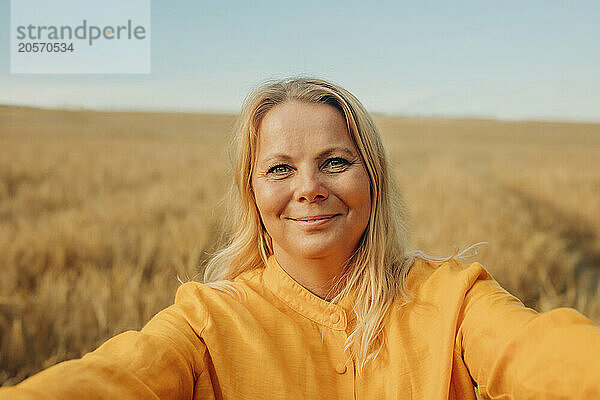 Smiling blond hair woman in yellow shirt on wheat field