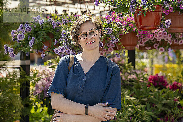 Smiling woman in eyeglasses with arms crossed standing in flower shop