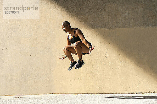 Determined sporty woman jumping in front of wall on sunny day