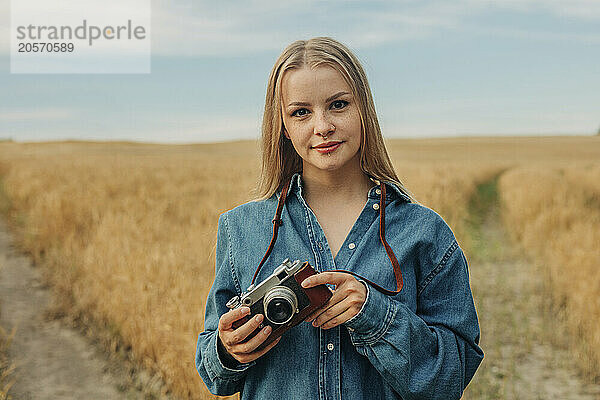 Blond hair woman holding camera and standing in wheat field