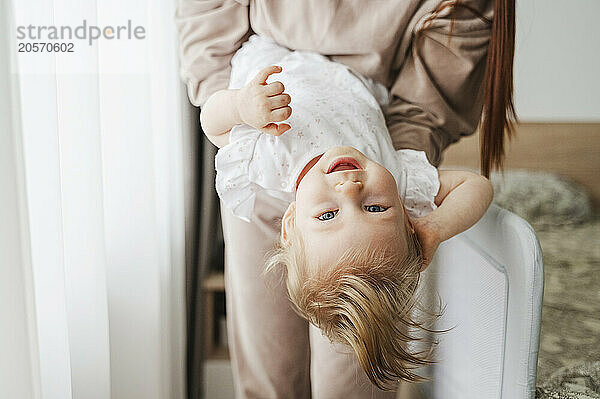 Mother holding daughter upside down in bedroom