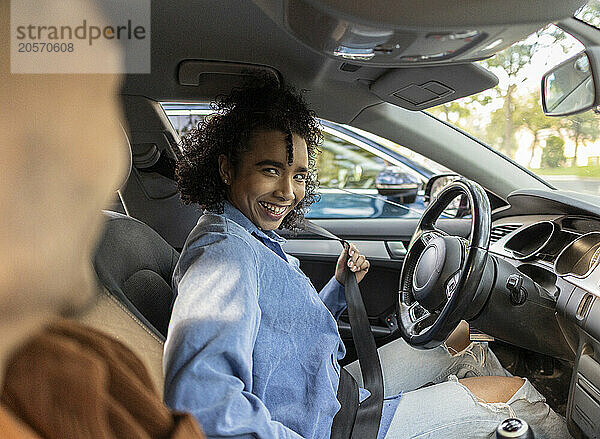 Happy woman fastening seat belt and sitting with boyfriend in car