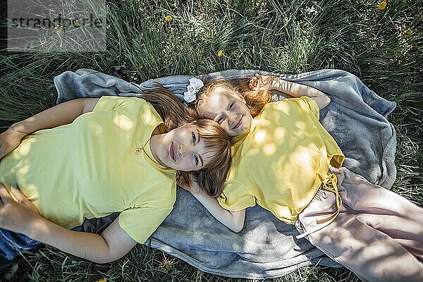 Happy mother and daughter lying on blanket in garden