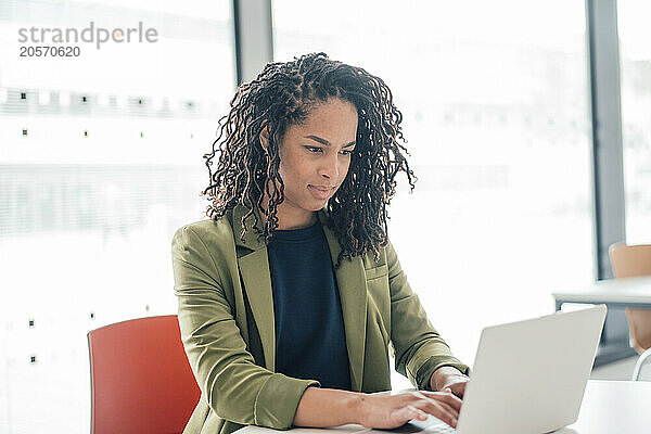 Confident young businesswoman using laptop at table in office cafeteria