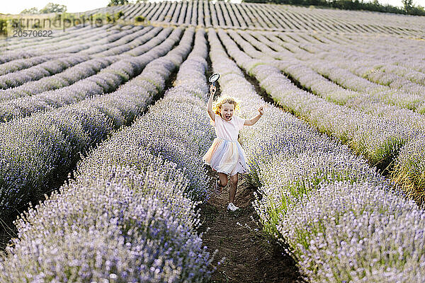 Carefree girl holding magnifying glass and running in lavender field