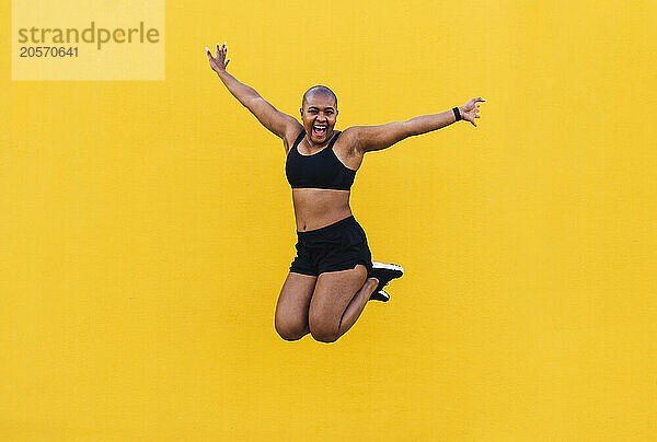 Cheerful woman jumping in front of yellow wall