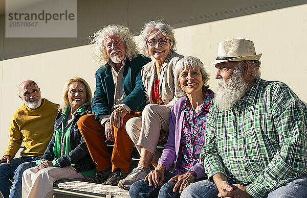 Happy retired men and women sitting together on bench in front of wall