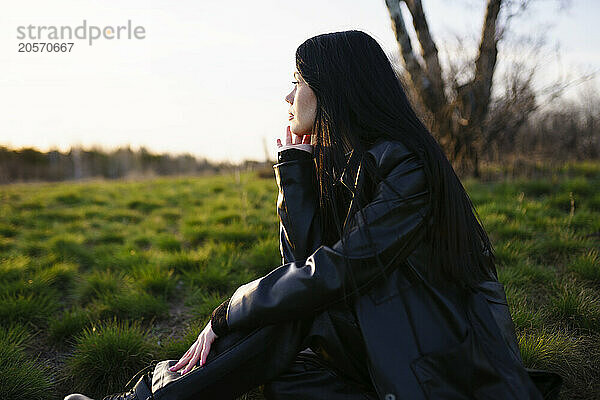 Young woman with hand on chin sitting in field on sunny day