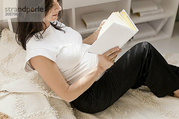 Pregnant woman sitting and reading book in bohemian room