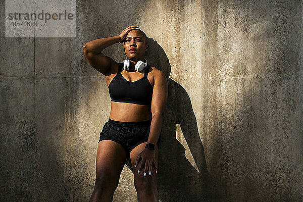 Tired sporty woman with hand on head leaning on wall