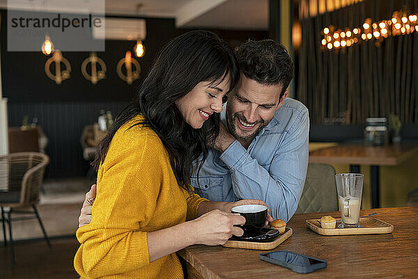 Happy businessman with businesswoman holding coffee cup at table in cafe