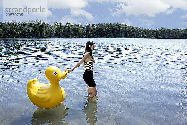 Girl pulling yellow rubber duck and walking in lake on sunny day