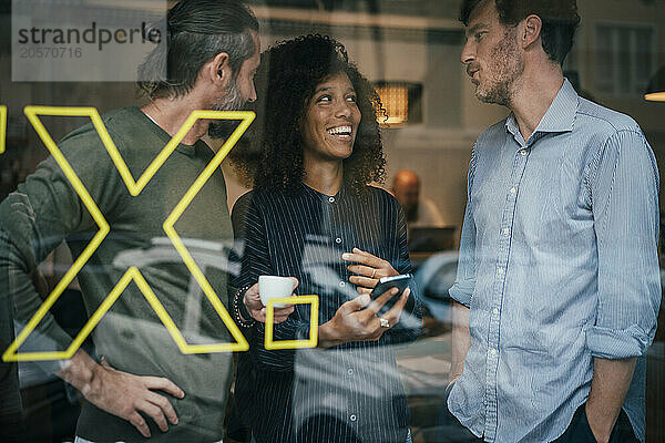 Happy business colleagues talking with each other in cafe seen through window