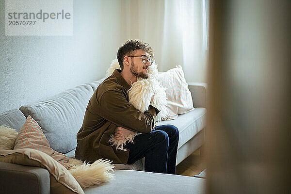 Relaxed young man hugging cushion sitting on sofa at home