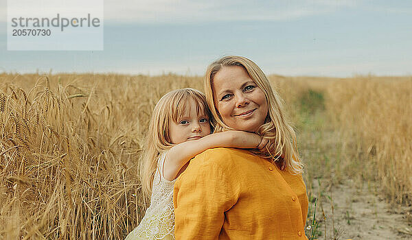 Cute girl with arm around mother at wheat field