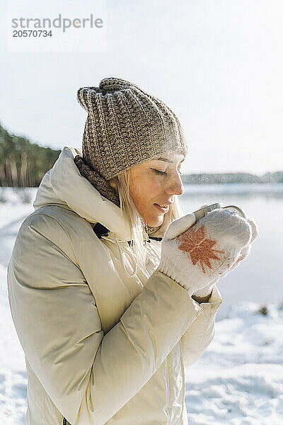 Woman wearing knit hat drinking hot tea in winter