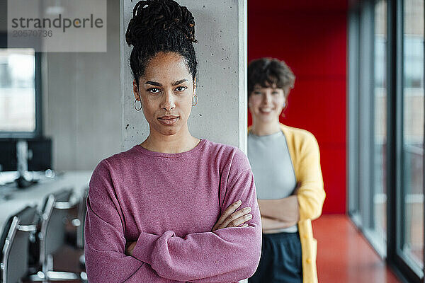 Confident entrepreneur with arms crossed in front of colleague in office