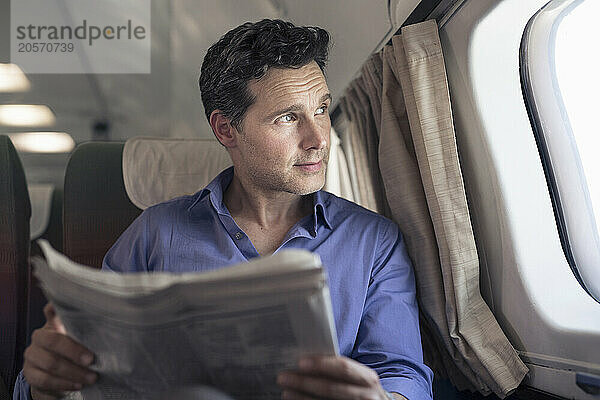 Confident mature businessman with newspaper looking out through airplane window