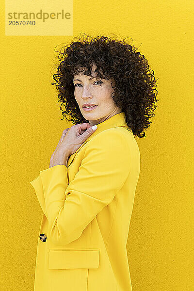 Confident beautiful woman wearing blazer in front of yellow wall